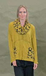 Load image into Gallery viewer, Front top half view of a woman wearing the Chalet Simone Top in the color marigold. This top has long sleeves, decorative criss-crossing seams and two front pockets with black circles on them.

