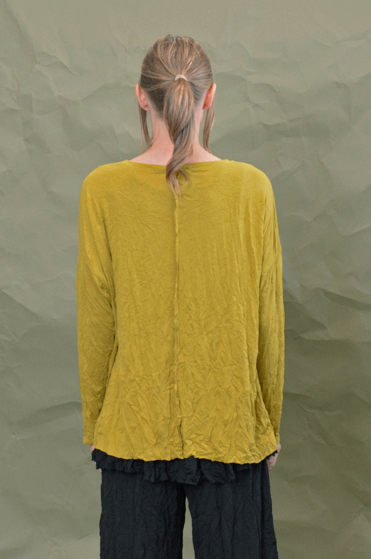 Back top half view of a woman wearing the Chalet Simone Top in the color marigold. This top has long sleeves and a long decorative seam running down the middle of the back.