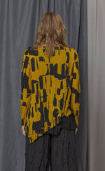 Load image into Gallery viewer, Back top half view of a woman wearing the chalet thora top. This top is gold and black with a geometric print. The top has long sleeves and an asymmetrical pointed hem.
