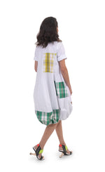 Load image into Gallery viewer, Back full body view of a woman wearing the alembika plaid wonderful dress. This dress is white with yellow, green, and brown plaid panelling/patches. The dress has short sleeves. The bottom is wide and full.
