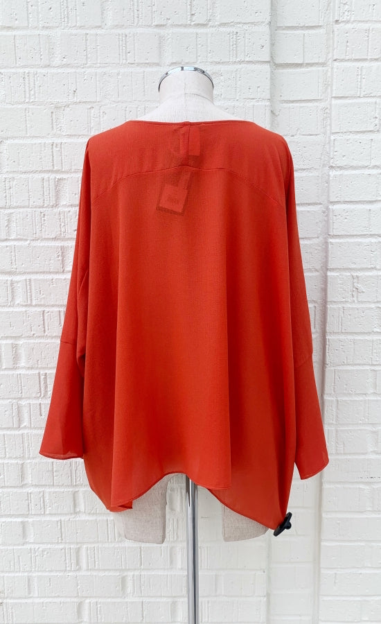 Back view of the crea concept orange top. This top has 3/4 length sleeves and a boxy silhouette