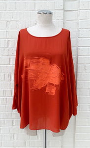 Front view of the crea concept orange top. This top has 3/4 length sleeves, a round neck, and a paint brush print in orange on the front.
