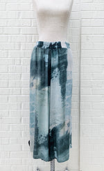 Load image into Gallery viewer, Front view of the crea concept abstract watercolor pant. This pant is wide legged and has a teal watercolor-like print on it. 
