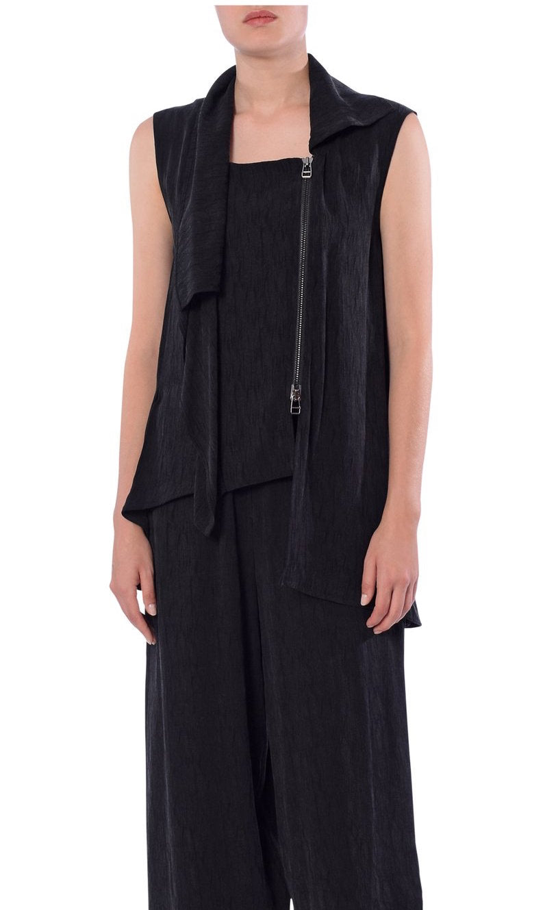 Front top half view of a woman wearing the crea concept black vest/top. This top is sleeveless with a draped front, a zipper on the front left side, and an asymmetrical hem.