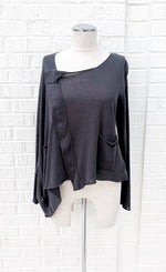 Load image into Gallery viewer, Front view of the crea concept knit cape top. This top is grey and semi-translucent. It has long sleeves, two patch front pockets, a right sided snap up front, and a cape feature over the right arm.
