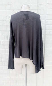 Back view of the crea concept knit cape top. This top is grey and semi-translucent. It has long sleeves and a cape like feature on the right side.