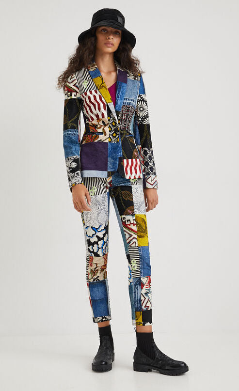 Front full body view of a woman wearing a hat and the desigual alejandra denim patch blazer. This blazer features a patchwork of multiple prints, a single button closure, a flat lapel, and long sleeves.