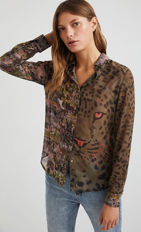 Front top half view of a woman wearing the desigual daytona wild print shirt. The base color of this shirt is green/brown. It has an animal print with a tiger face on the left side and a mixed watercolor print on the right side. The shirt has a button up front and long sleeves with cuffs.