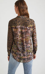 Load image into Gallery viewer, Back top half view of a woman wearing the desigual daytona wild print shirt. The base color of this shirt is green/brown. It has an animal print on shoulders and sleeves and a mixed watercolor print on back. 
