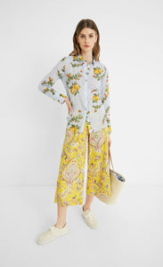 Front full body view of a woman wearing yellow paisley capris and the desigual lemons cotton shirt. This shirt is blue with lemons printed on it. The top has a button down front, a shirt collar, and long sleeves.