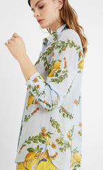 Load image into Gallery viewer, Left side top half view of a woman wearing yellow paisley capris and the desigual lemons cotton shirt. This shirt is blue with lemons printed on it. The top has a button down front, a shirt collar, and long sleeves.
