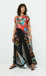 Load image into Gallery viewer, Front full body view of a woman wearing the desigual postcards short sleeve t-shirt. This top is red with tropical post cards all over it and flowers. The top has short sleeves, a round neck, and a rounded hem.
