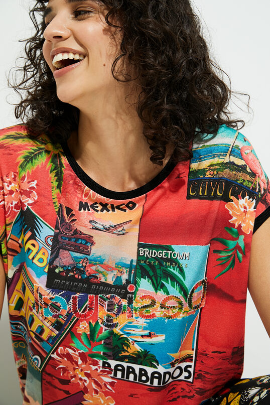 Front close up view of a woman wearing the desigual postcards short sleeve t-shirt. This top is red with tropical post cards all over it and flowers. The top has short sleeves and a round neck.
