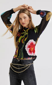 Front top half view of a woman wearing the desigual babel floral blouse. This blouse is black with a floral print on it. The body is fitted and shirred/ruffled-like. The sleeves are made of transparent fabric and are wide with a shirred cuff. 