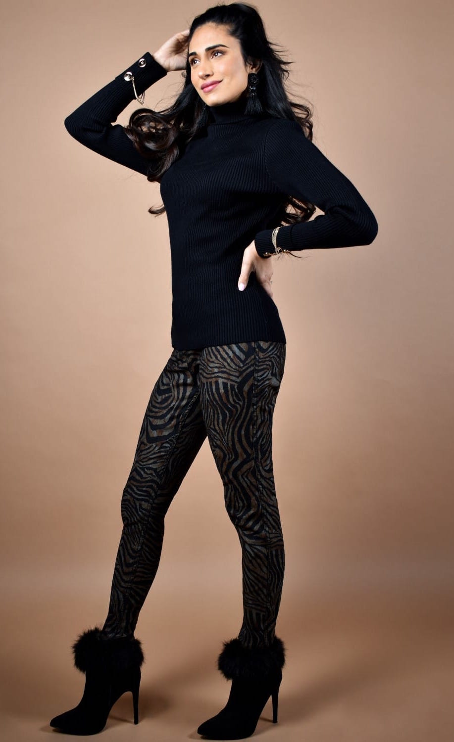 Front full body view of a woman wearing a black sweater and the frank lyman reversible zebra/black pant. This side of the pant is brown and black zebra print. The pants are slim fitting.