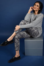 Load image into Gallery viewer, Front full body view of a woman sitting and wearing the frank lyman grey knit sweater. This solid sweater has long sleeves with a braided detail running down the sides. 
