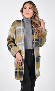 Front top half view of a woman wearing the frank lyman plaid sweater jacket. This jacket is open over a grey turtleneck and the model is wearing it with black sweatpants. The grey and mustard jacket has long sleeves and two front patch pockets.