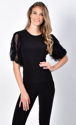 Load image into Gallery viewer, Front view of a woman with one hand on her hip and wearing a black jersey knit top with sheer sleeves from Frank Lyman. The sheer sleeves are ruffled and 3/4 length.

