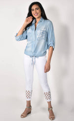 Load image into Gallery viewer, Front full body view of a woman wearing white pants and the frank lyman blue amore shirt. This shirt has a button down front, a drawstring hem with a tie in the middle, and two front patch pockets. The right pocket has sequins on it while the left pocket has words about love written on it.
