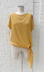 Load image into Gallery viewer, Front view of a mannequin wearing a marigold woven top from Frank Lyman with short sleeves and a front side tie at the bottom.
