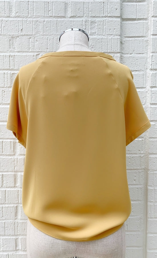 Front view of a mannequin wearing a marigold woven top from Frank Lyman with short sleeves.
