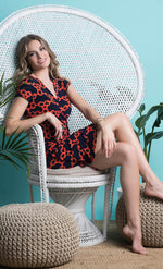 Load image into Gallery viewer, woman sitting on a wicker chair with her legs crossed and wearing a navy and orange short sleeve chain print wrap dress from Frank Lyman
