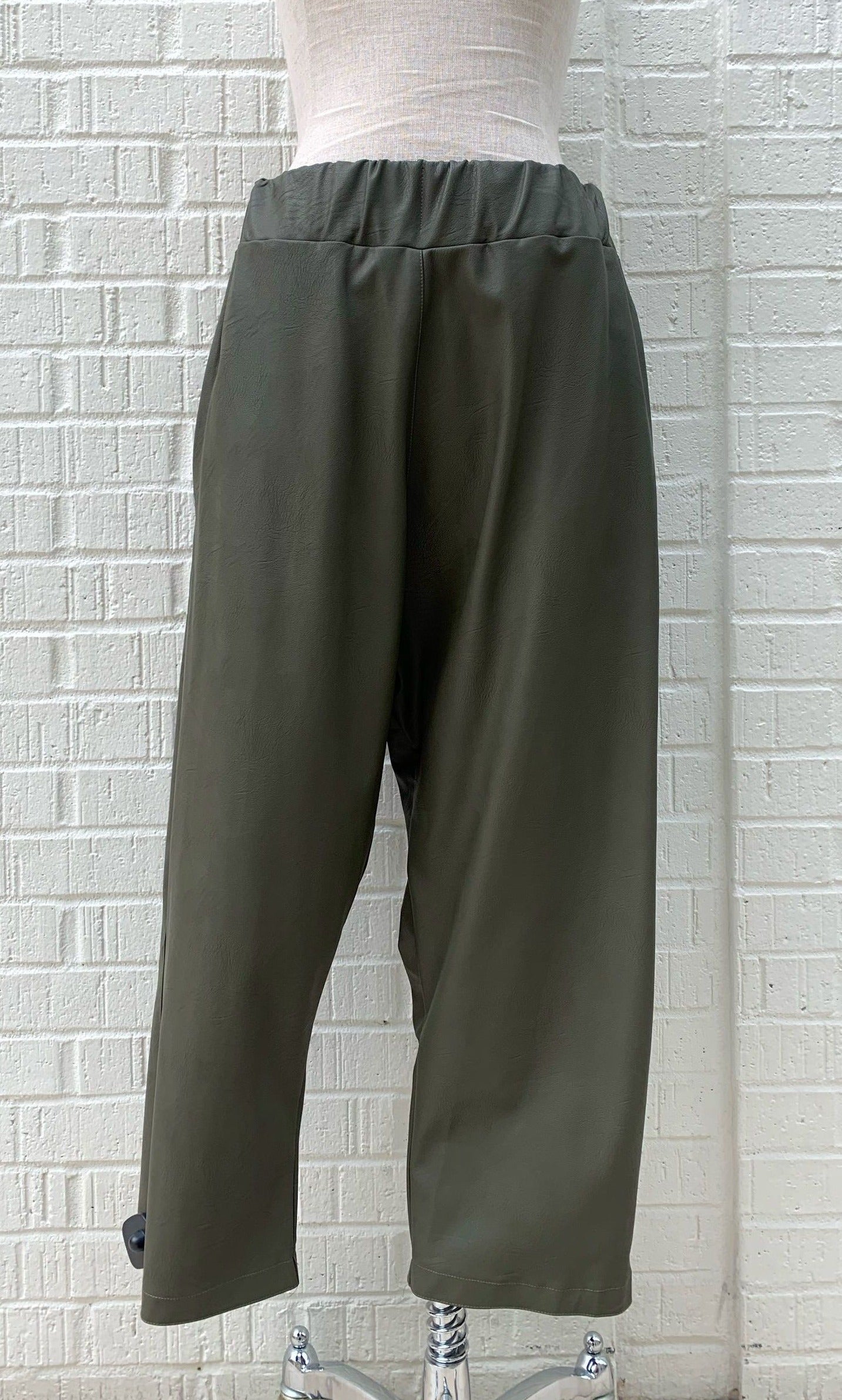 Front bottom half view of the hashtagmart green crop pant. This pant has an elastic waistband, a wide leg, and a drop crotch. The looks like leather.