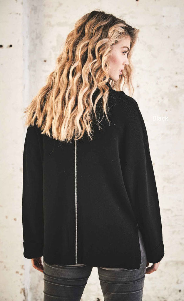 Back top half view of a woman wearing the henry christ double check sweater in black. This sweater has long sleeves with folded cuffs, a cowl neck, and contrasting metallic silver stitching running down the middle of the back