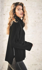 Load image into Gallery viewer, Right side upper body view of a woman wearing the henry christ double check sweater in black. This sweater has long sleeves with folded cuffs, a cowl neck, and contrasting metallic silver stitching running down the side.
