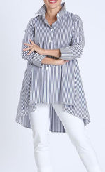 Load image into Gallery viewer, Front top half view of a woman wearing white pants and the IC Collection Navy Striped Shirt. This shirt has vertical navy and white stripes in the front and on the arms with diagonal stripes on the side. The shirt has cuffed 3/4 length sleeves, a button down front, and a shirt collar.
