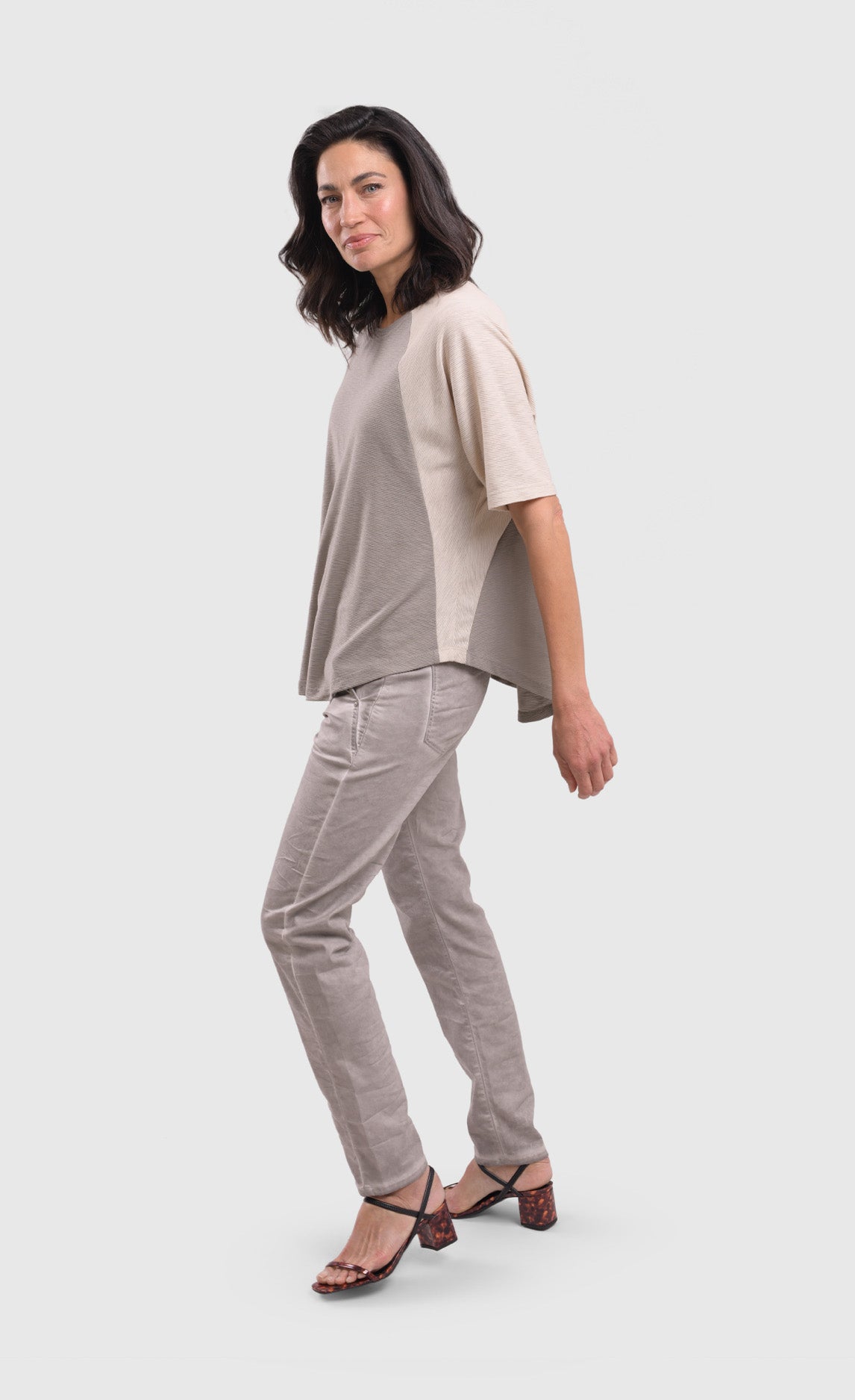 Left side full body view of a woman wearing a grey alembika top and the alembika grey iconic stretch jeans. These light grey jeans have two front and back pockets and a relaxed slim/straight cut.