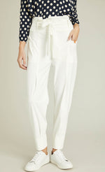Load image into Gallery viewer, Front bottom half view of a woman wearing a blue and white polka dot top and the indies white collin pants. These pants have a carrot shape, two front patch pockets, and a tie belt.

