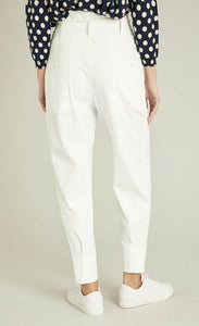 Back bottom half view of a woman wearing a blue and white polka dot top and the indies white collin pants. These pants have a carrot shape, two back patch pockets, and a tie belt.