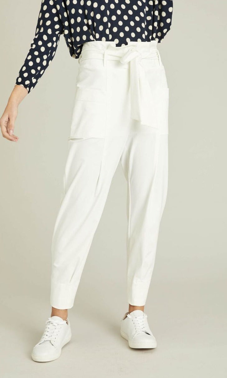 Front full body view of a woman wearing a blue and white polka dot top and the indies white collin pants. These pants have a carrot shape, two front patch pockets, and a tie belt.