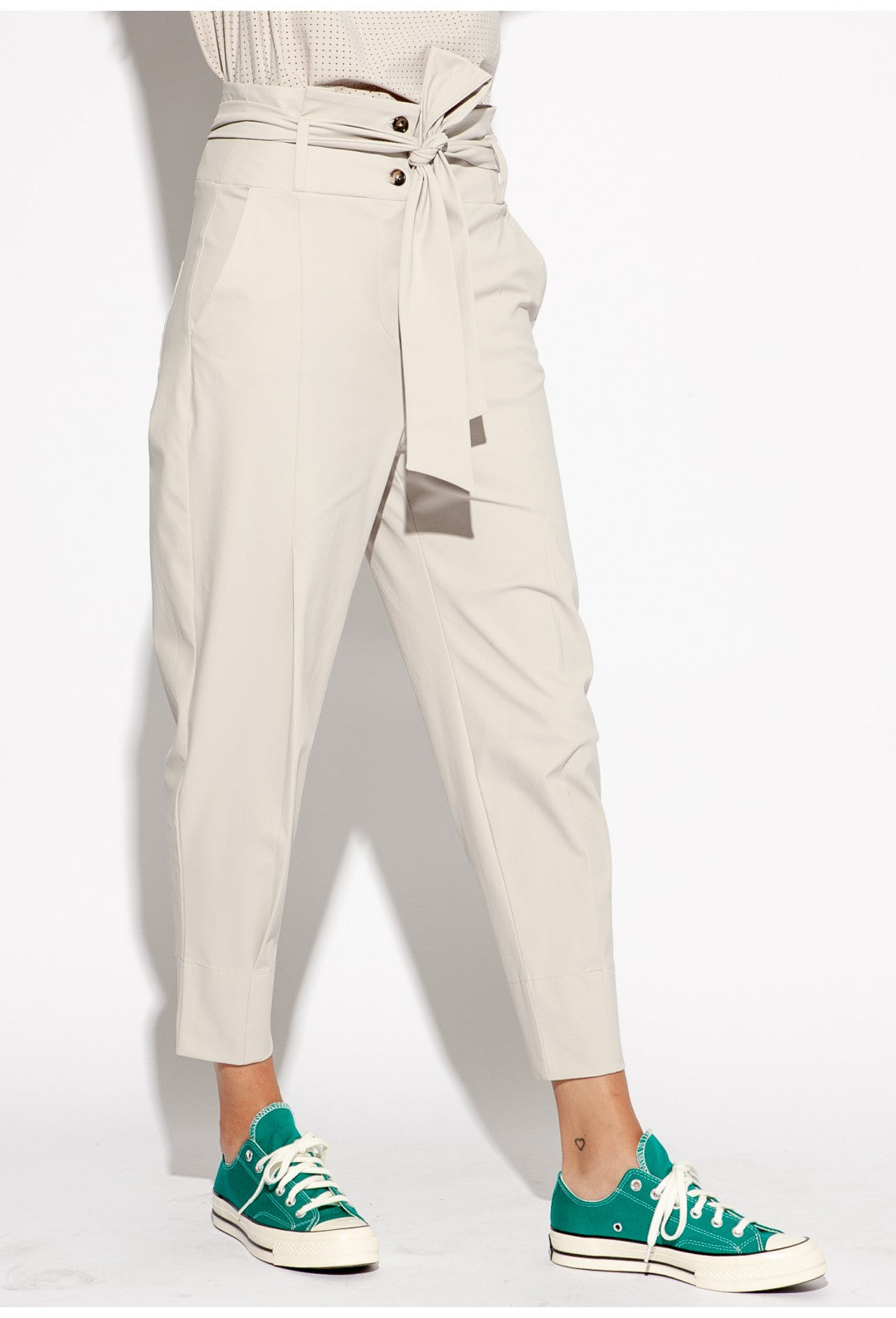 Front right side bottom half view of a woman wearing the Indies Collin Pant. This pant is pebble/beige colored with a straight leg and a high rise waistband with a belt.