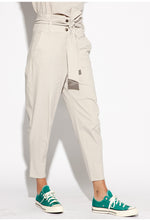 Load image into Gallery viewer, Front right side bottom half view of a woman wearing the Indies Collin Pant. This pant is pebble/beige colored with a straight leg and a high rise waistband with a belt.
