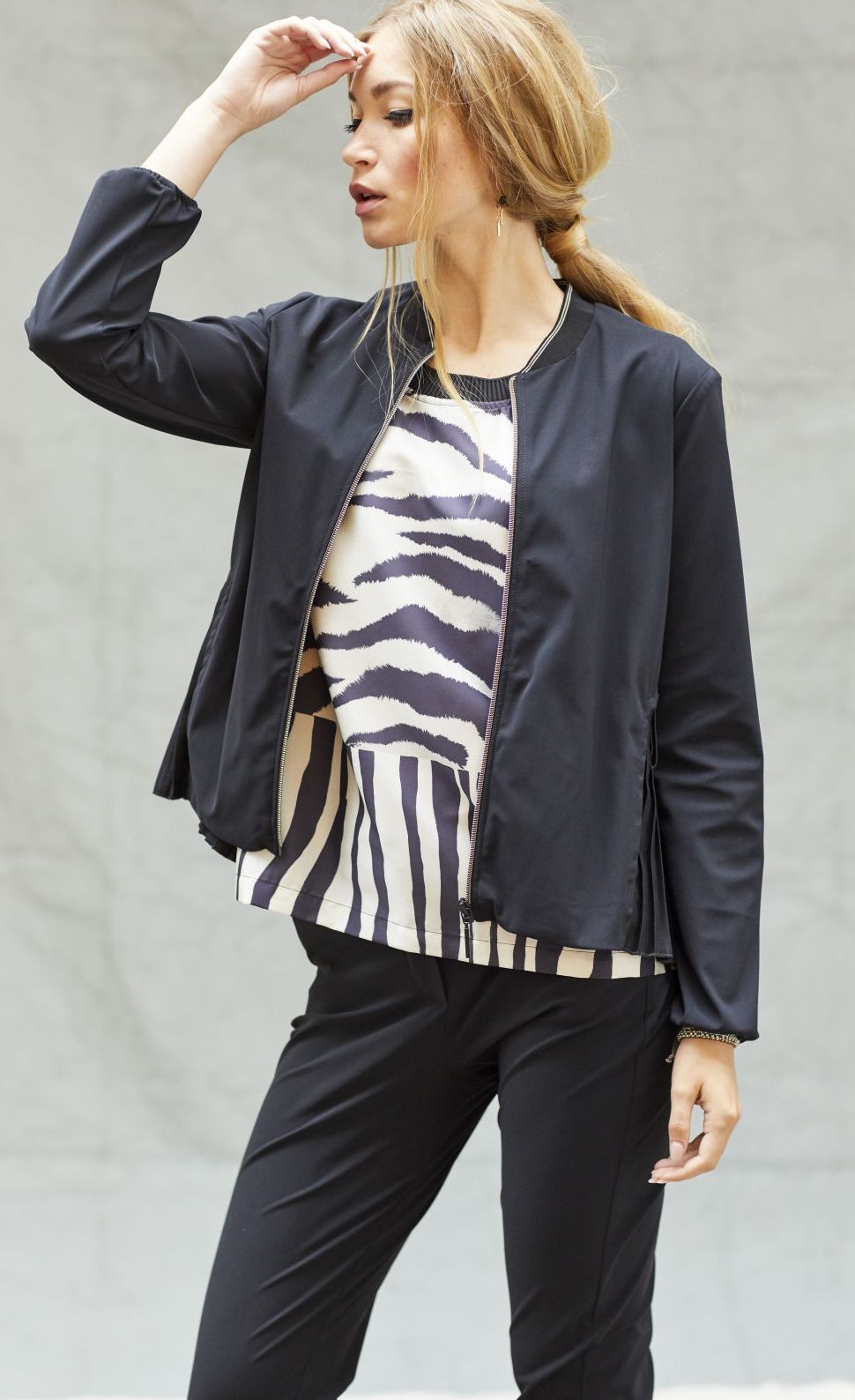 Front top half view of a woman wearing black pants, and black and white tank with the indies black fute jacket over it. This jacket has a zip front, long sleeves, and a short collar.