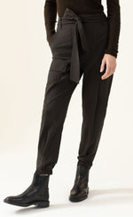 Load image into Gallery viewer, Front bottom half view of a woman wearing the indies luna kaki pant. These pants have a large waistband with a tie belt, front patch pockets, a relaxed fit, and a tapered elastic hem.
