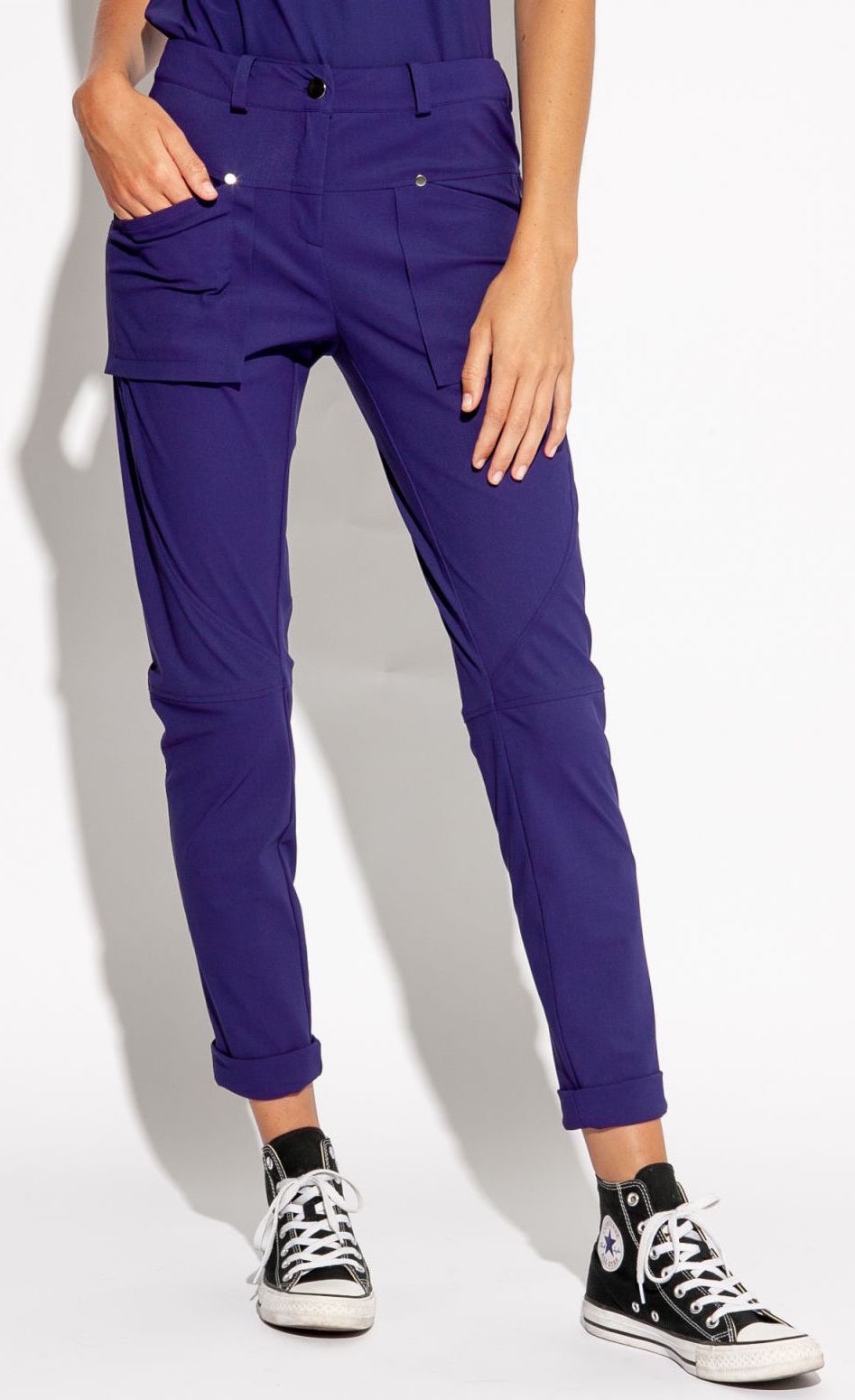 Front bottom half view of a woman wearing the indies nico pant in the color indigo. This pant has two front patch pockets. The model has her hand in the right front pocket. The pant also has seams on the knees and a cuffed hem that ends above the ankles.