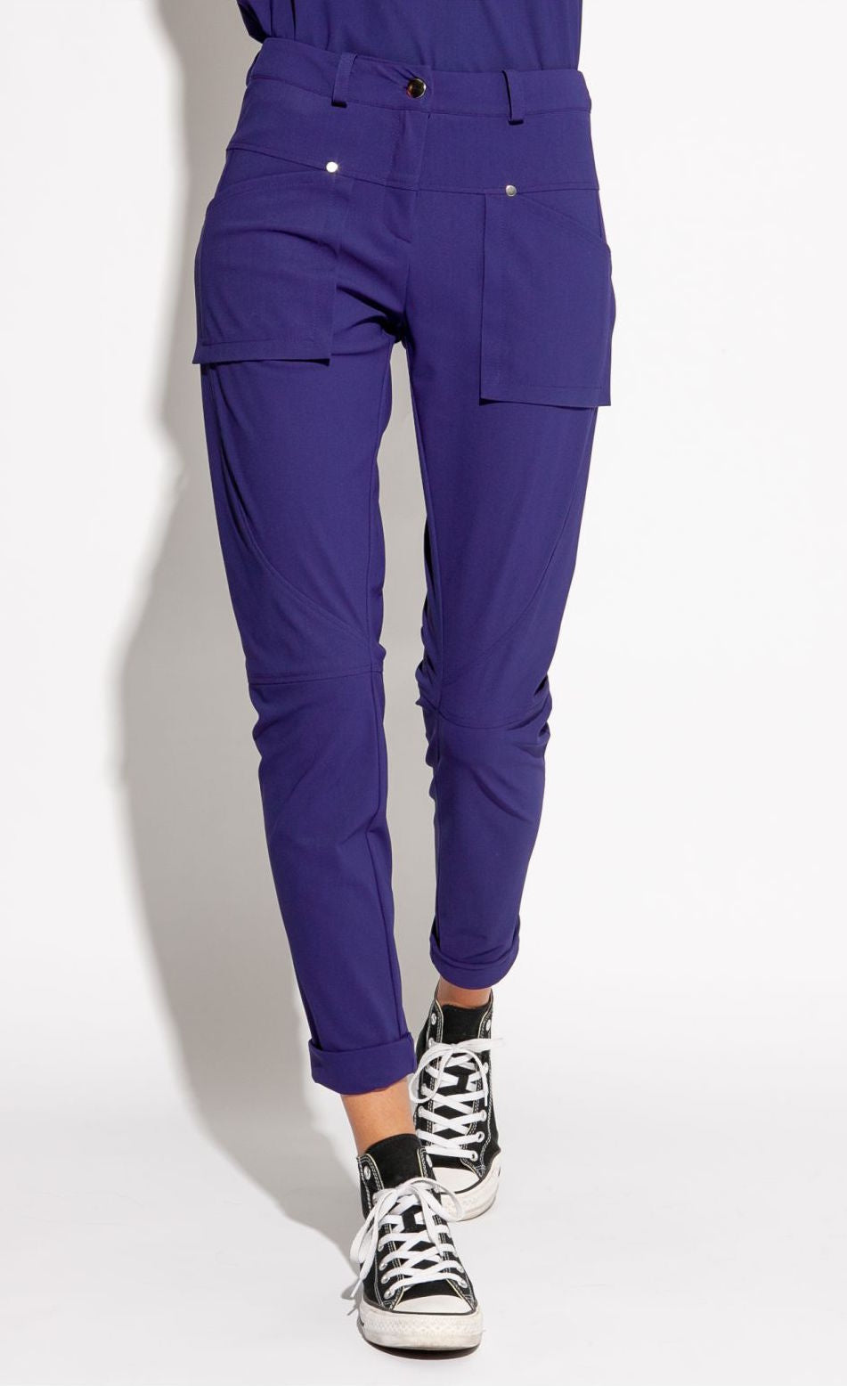 Front bottom half view of a woman wearing the indies nico pant in the color indigo. This pant has two front patch pockets. The pant also has seams on the knees and a cuffed hem that ends above the ankles.