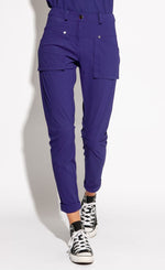 Load image into Gallery viewer, Front bottom half view of a woman wearing the indies nico pant in the color indigo. This pant has two front patch pockets. The pant also has seams on the knees and a cuffed hem that ends above the ankles.
