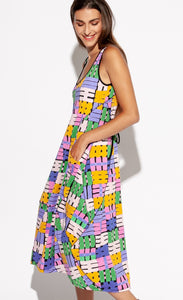 Front full body view of a woman wearing the Indies Nils Dress. This dress has multicolored hashtags printed all over it. It is sleeveless with a round neckline that is lined with black trim. The dress sits below the knees but above the ankles. The model has her hands in the front pockets. 