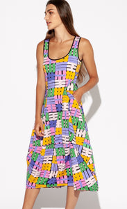 Front full body view of a woman wearing the Indies Nils Dress. This dress has multicolored hashtags printed all over it. It is sleeveless with a round neckline that is lined with black trim. The dress sits below the knees but above the ankles. The model has her hand in the front pocket.