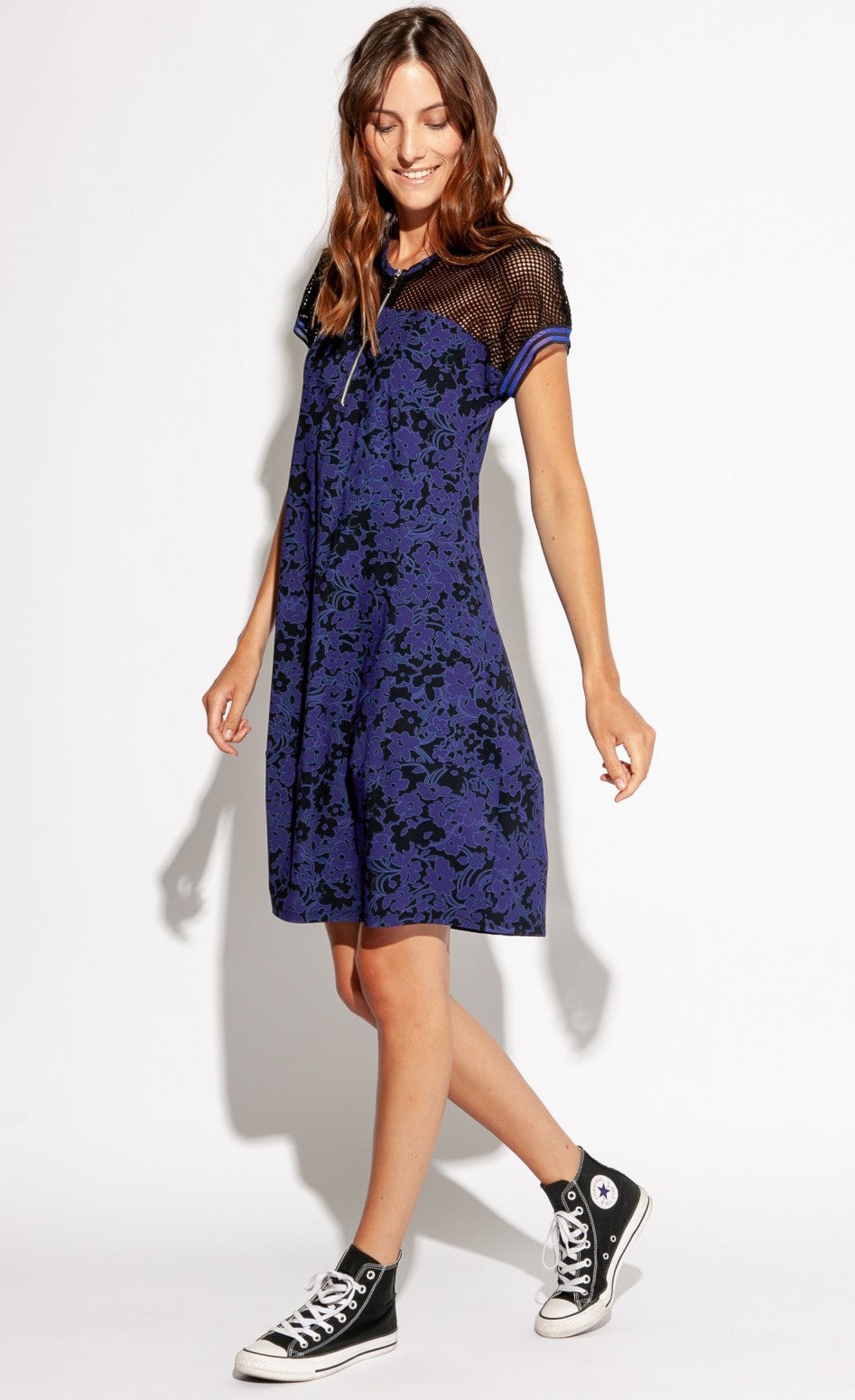Front left sided full body view of a woman wearing the Indies Skipy Dress. This dress is indigo blue and black with a floral print and black mesh on the shoulders and short sleeves. The dress is loose fitting with a slightly fitted waist and a cut that sits above the knees.