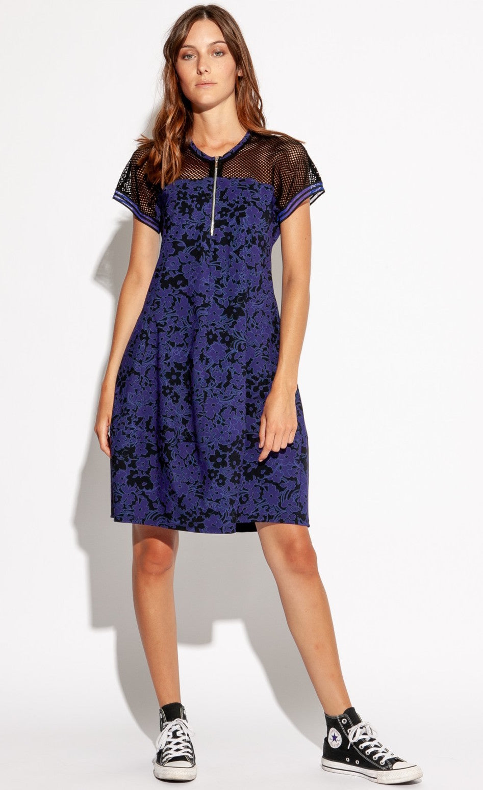 Front full body view of a woman wearing the Indies Skipy Dress. This dress is indigo blue and black with a floral print and black mesh on the shoulders and short sleeves. The dress is loose fitting with a slightly fitted waist and a cut that sits above the knees.