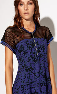 Front close up torso view of a woman wearing the Indies Skipy Dress. This dress is indigo blue and black with a floral print and black mesh on the shoulders and short sleeves. The dress has a short zipper near the neckline.