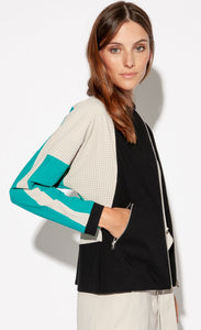 Ride side top half view of a woman with her hand in the pocket of the Indies Nano Jacket. The jacket has a black front, a seafoam blue sleeve, and beige/pebble colored, perforated sleeves.