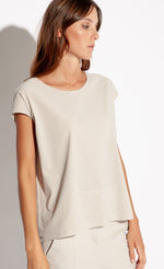 Load image into Gallery viewer, Front top half view of a woman wearing pebble/beige colored pants and the Indies Cara Tee-Shirt. The Tee-shirt is also pebble/beige. It has perforated fabric, cap sleeves, and a relaxed fit.
