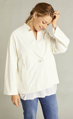 Load image into Gallery viewer, Front top half view of a woman wearing blue jeans and the white indies voyageur jacket. This jacket is closed and layered over a white top. The jacket has a single front button, long sleeves, and a flared fit.
