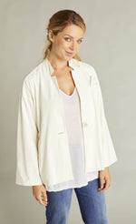 Load image into Gallery viewer, Front top half view of a woman wearing blue jeans and the white indies voyageur jacket. This jacket is open and layered over a white top. The jacket has a single front button, long sleeves, and a flared fit.
